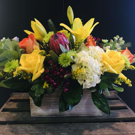 Mixed bouquet with yellow lilies, roses, hydrangea, and protea in a wooden box