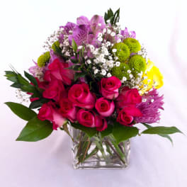 Mixed bouquet of pink roses, purple alstroemeria, and green pompons in a glass vase