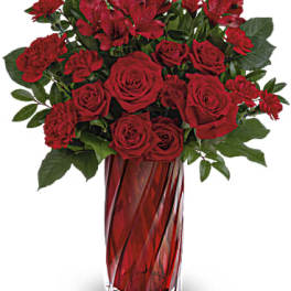 Tall bouquet of red roses, carnations, and alstroemeria in a red glass vase