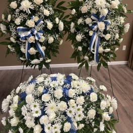 Three white floral funeral sprays with blue ribbons and stands