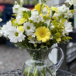 Yellow and white daisies in a clear glass pitcher vase