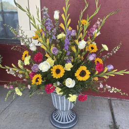 Tall mixed flower arrangement in a gray urn with sunflowers and roses