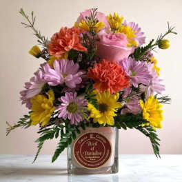 Mixed pink, yellow, and orange flowers arranged in a glass candle jar