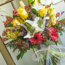 Bouquet of yellow roses, white calla lilies, and pink gerbera daisies in a glass vase