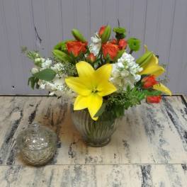 Bouquet of yellow lilies, orange roses, and white flowers in a glass vase