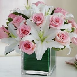 Pink roses and white lilies arranged in a clear square vase