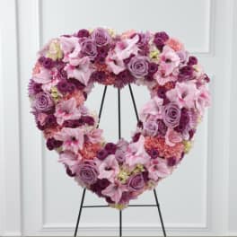 Heart-shaped floral wreath in pink and purple tones on a black stand