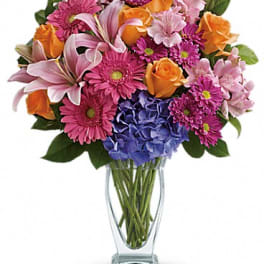 Mixed bouquet of pink, orange, and purple flowers in a clear glass vase