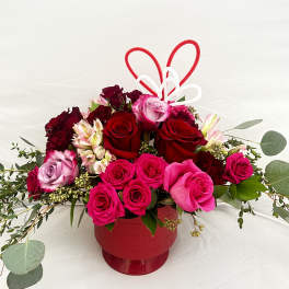 Red and pink roses arranged in a red vase with heart picks