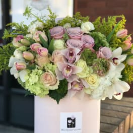 Pastel bouquet of roses, orchids, and hydrangeas in a pink hatbox
