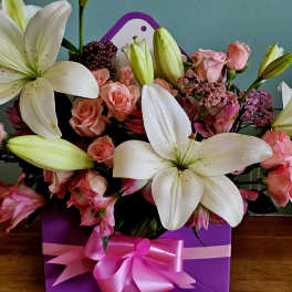 Pink roses and white lilies arranged in a purple gift box with a pink ribbon