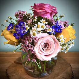 Mixed bouquet of pink and yellow roses with small daisy flowers in a glass vase