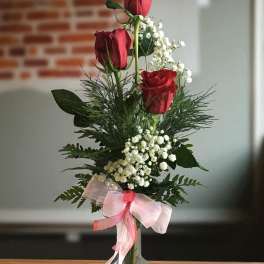 Tall vase arrangement with red roses, baby's breath, and a pink ribbon