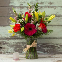 Mixed bouquet of red roses, pink gerbera daisies, and yellow lilies in a glass vase