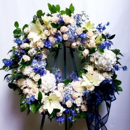 Large floral wreath with white lilies, cream roses, blue flowers, and a navy ribbon