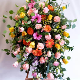 Large mixed flower arrangement on an easel with pink, yellow, and orange blooms