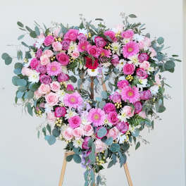 Heart-shaped floral wreath of pink roses and daisies on a wooden stand