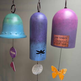 Three colorful hanging wind chimes with bell-shaped tops and dangling charms