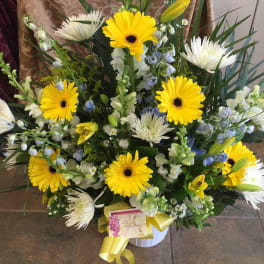 Yellow gerberas and white lilies in a white vase with a yellow ribbon