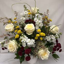 Tall arrangement of ivory roses, white stock, yellow button mums and burgundy mums in a white vase
