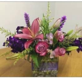 Pink lilies and roses in a glass vase with purple accents