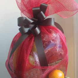Gift basket wrapped in red mesh with a black bow, topped with fruit