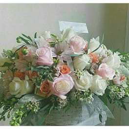 Pastel roses and white blooms arranged in a white basket