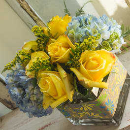 Yellow roses and blue hydrangeas in a square glass vase