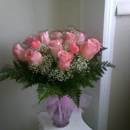 Pink roses arranged in a vase with baby's breath and a pink ribbon