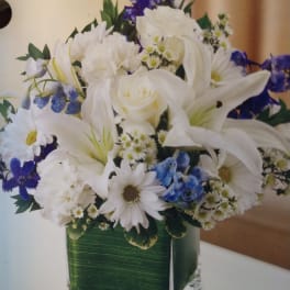 White lilies and daisies with blue flowers in a square glass vase