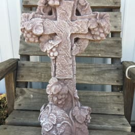 A pink stone cross with floral carvings sits on a wooden chair.