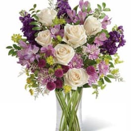 White roses and purple flowers in a clear glass vase