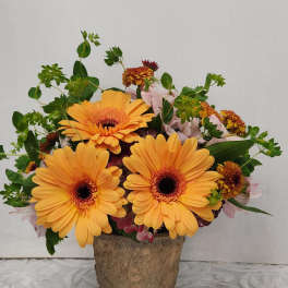 Orange gerbera daisies in a rustic vase with pink accent flowers