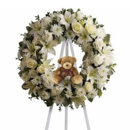 White floral wreath on an easel with a teddy bear in the center