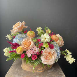 Mixed bouquet of peach roses, pink blooms, and blue flowers in a wooden container