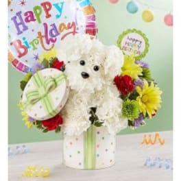 White teddy bear surrounded by colorful flowers and birthday balloons