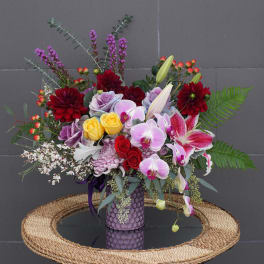 Mixed bouquet in a purple vase with orchids, lilies, roses, and dahlias