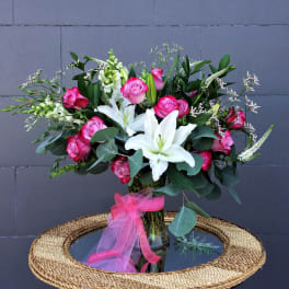 Pink roses and white lilies in a glass vase with a pink ribbon