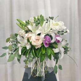 White lilies and roses in a glass vase with purple orchids