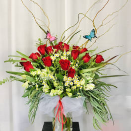 Tall bouquet of red roses and white flowers in a glass vase with butterfly picks