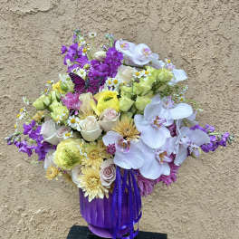 Mixed bouquet in a purple vase with orchids, roses, and daisies