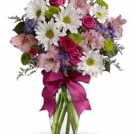 Bouquet of daisies, pink roses, and alstroemeria in a glass vase with a magenta ribbon