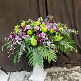 Large floral arrangement with purple and green flowers in a white pedestal vase