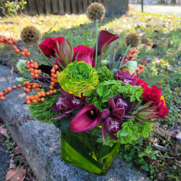 Colorful mixed bouquet in a green glass vase with calla lilies and orchids
