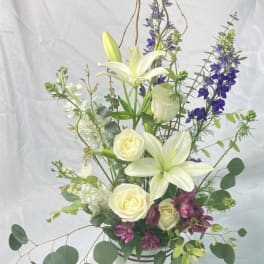 Tall white lily and rose arrangement with purple accents in a striped vase
