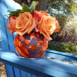 Orange roses in a pumpkin-shaped vase on a blue railing