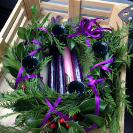 Evergreen wreath with purple ribbon and candle holders in a wooden crate