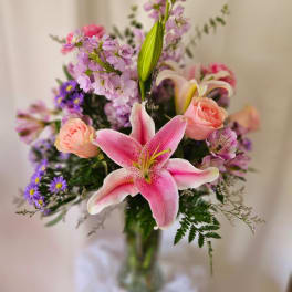 Pink lily bouquet with roses and purple filler flowers in a glass vase