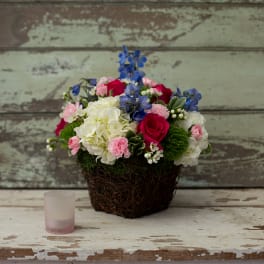 Mixed bouquet in a woven basket with roses, hydrangeas, and blue flowers