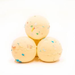 Three pale yellow bath bombs with colorful speckles stacked in a pyramid
